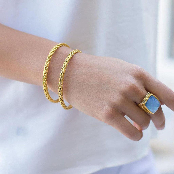 Gold braided bangle bracelets on a wrist, styled with a statement ring.