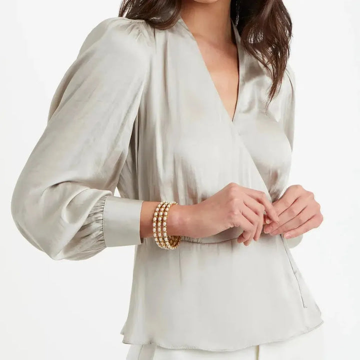 Triple-strand pearl bracelet on a model wearing a satin blouse.