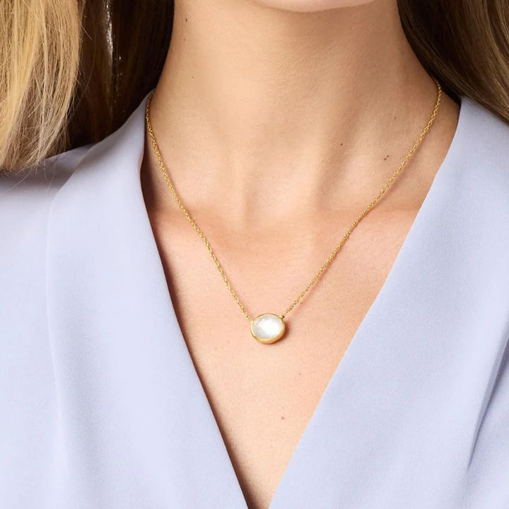 Gold chain necklace featuring a  white gemstone pendant on a lavender blouse.