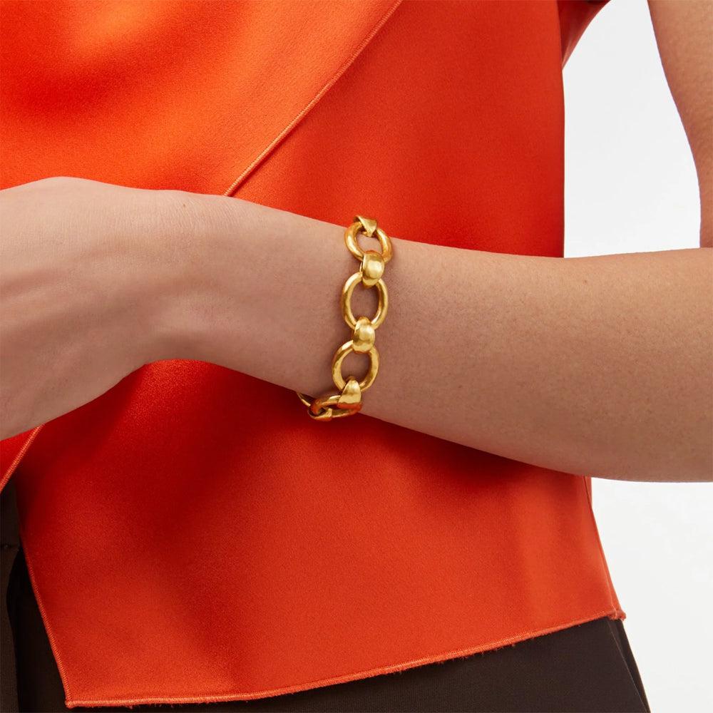 Gold link bracelet on a wrist, against a burnt orange background.