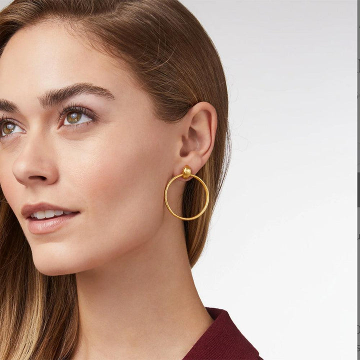 Gold doorknocker hoop earrings on a woman's ear.