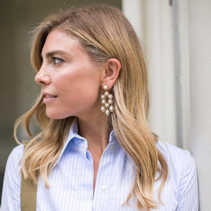 Gold and pearl statement earrings worn by a blonde woman in a blue striped shirt.
