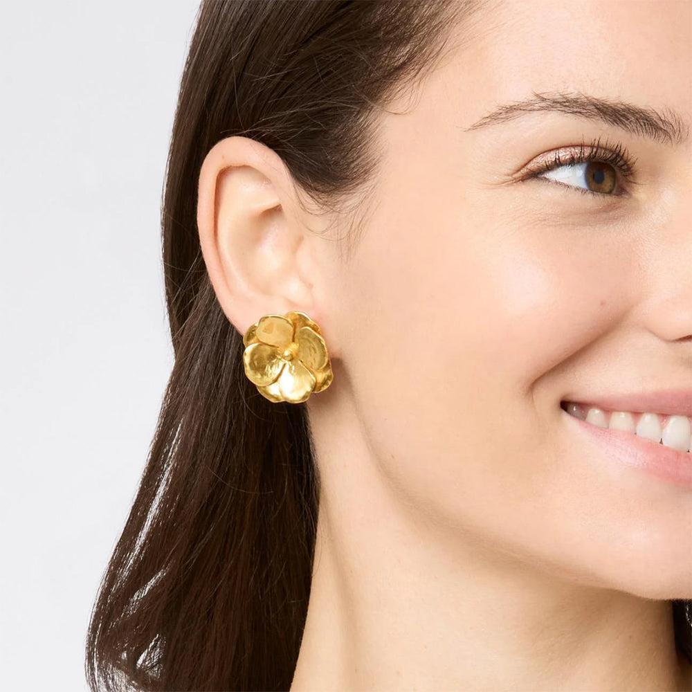 Gold flower-shaped clip earrings worn by a woman.