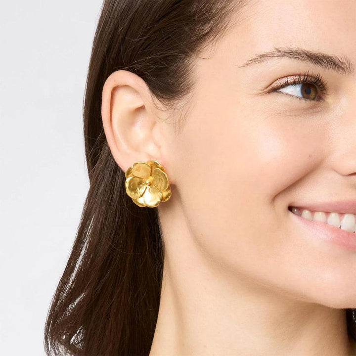 Gold flower-shaped clip earrings worn by a woman.