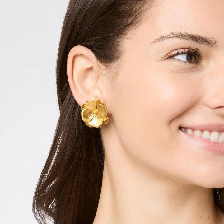 Gold flower-shaped stud earrings on a woman's ear.