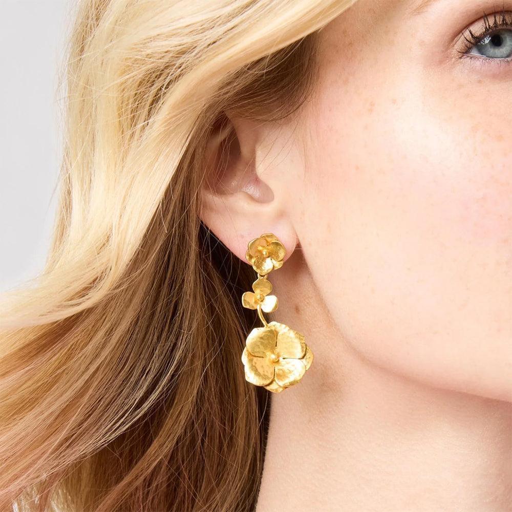 Gold flower drop earrings on model with blonde hair.