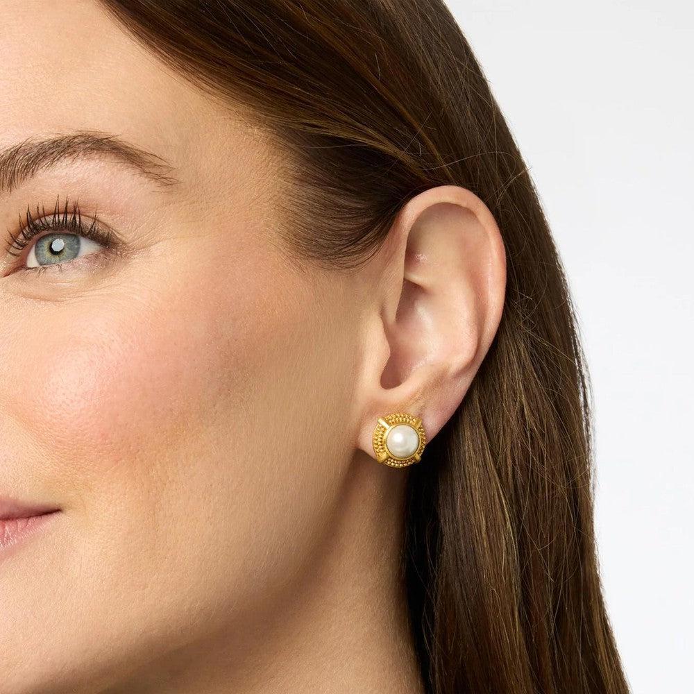 Gold-toned stud earrings featuring a white pearl center, shown on a woman's ear.