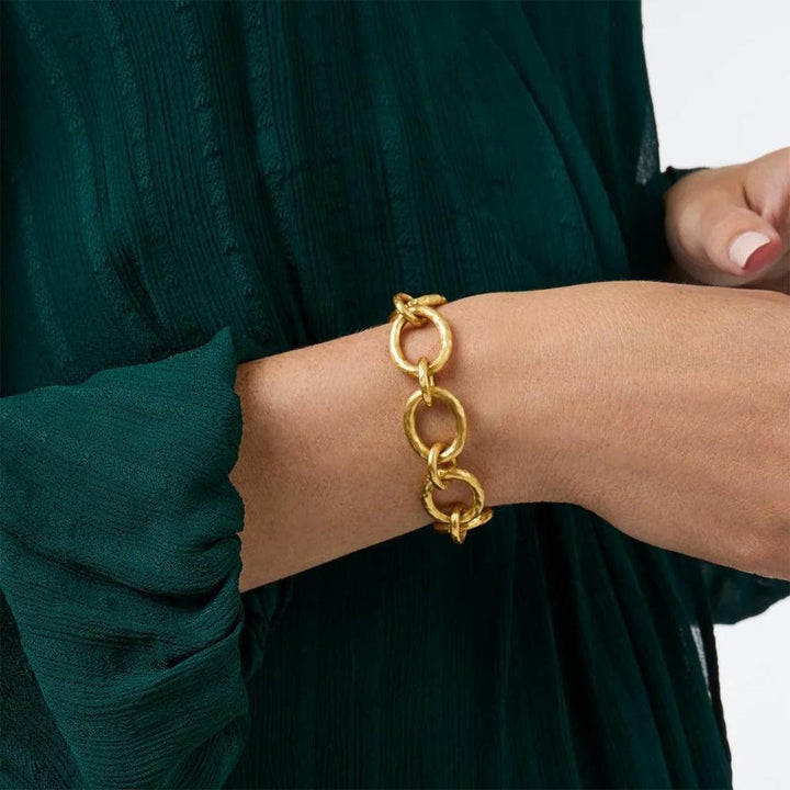 Gold hammered link bracelet on a wrist wearing a dark green sleeve.