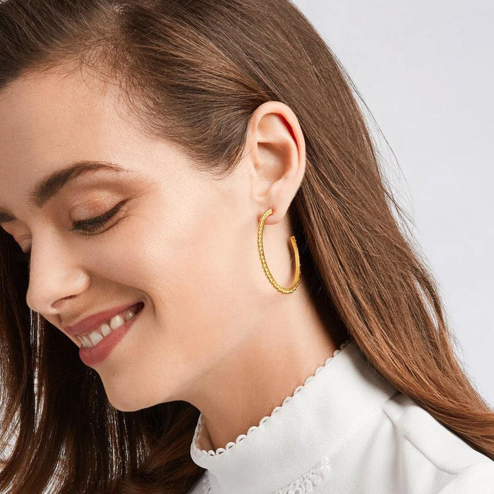 Gold textured hoop earrings on a woman's ear.