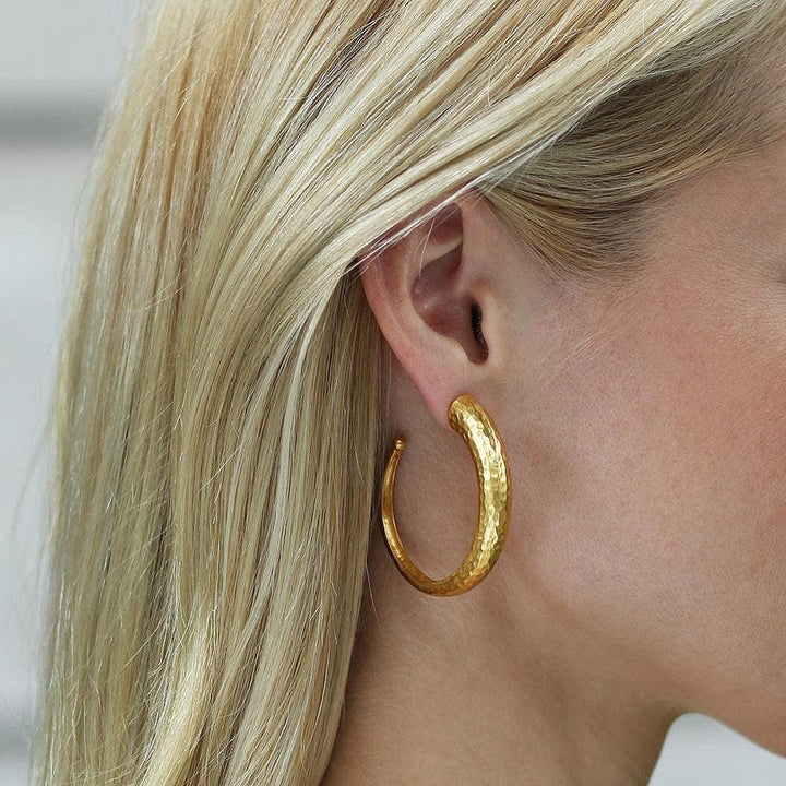 Gold hammered hoop earrings on model with blonde hair.