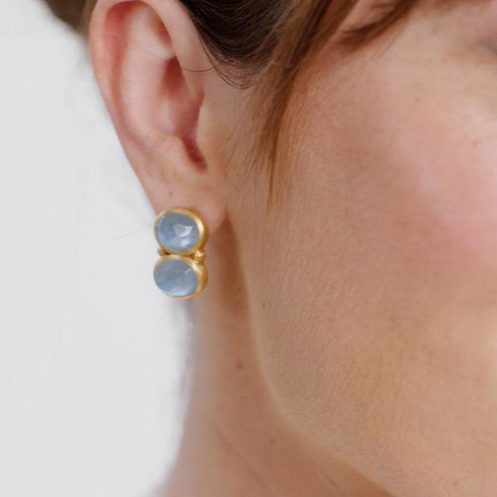 Blue gemstone earrings with gold settings, worn on earlobe.