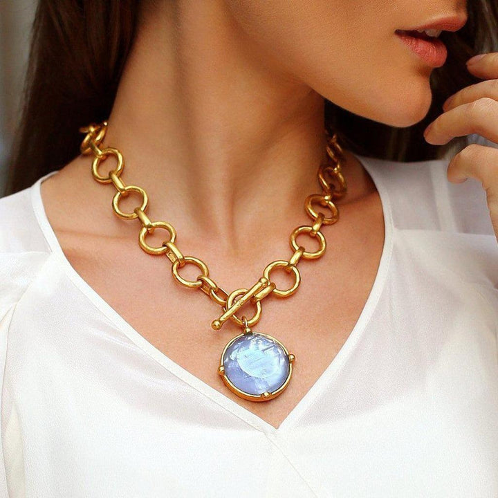 Gold statement necklace with a large, pale blue stone pendant.