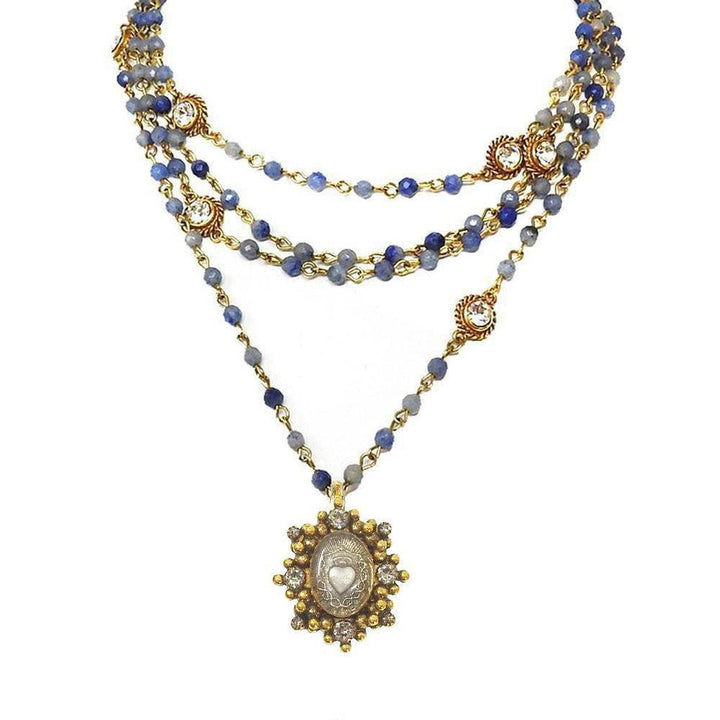 Layered blue gemstone and gold necklace with ornate heart pendant.