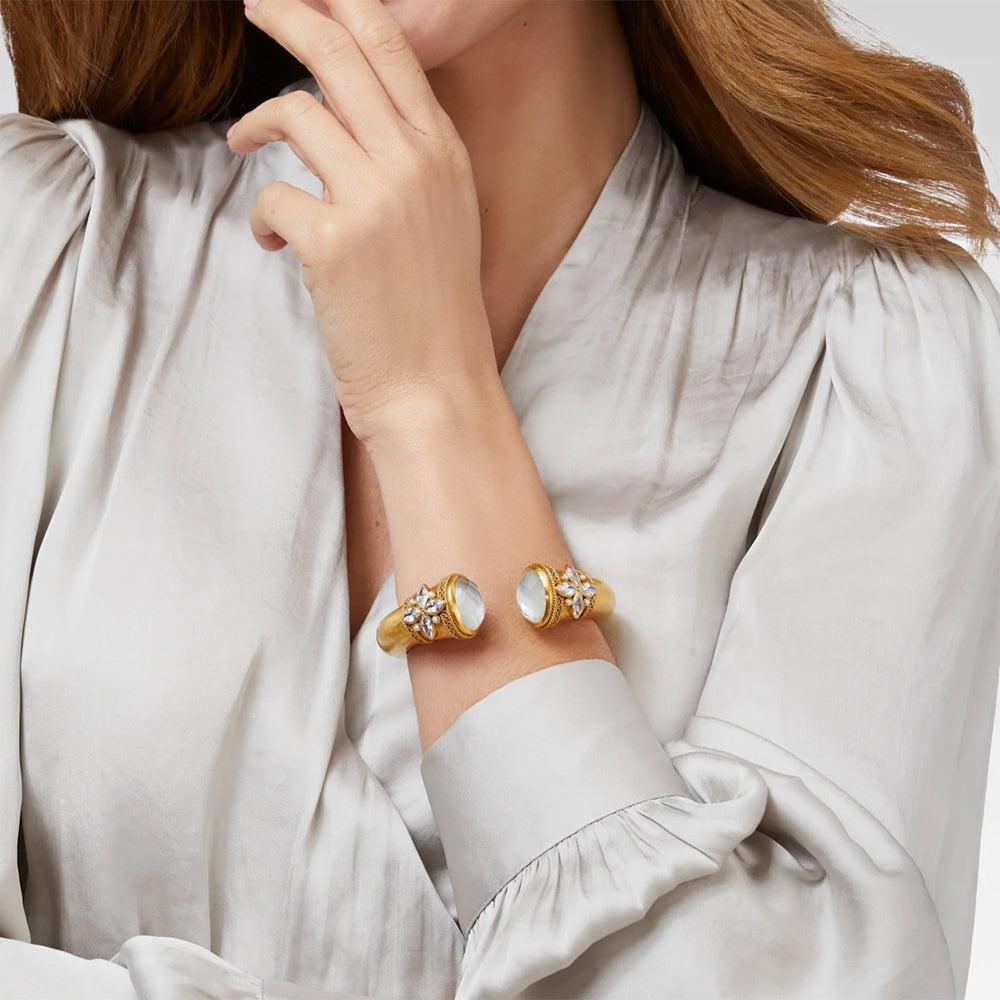 Gold cuff bracelet with opal accents, worn on a model's wrist.