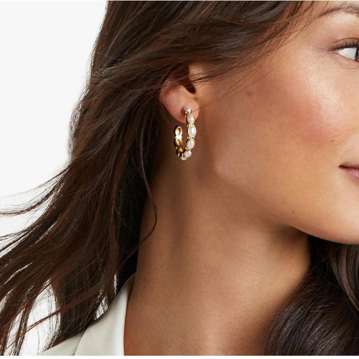 Gold hoop earrings adorned with oval pearls, worn against a white backdrop.