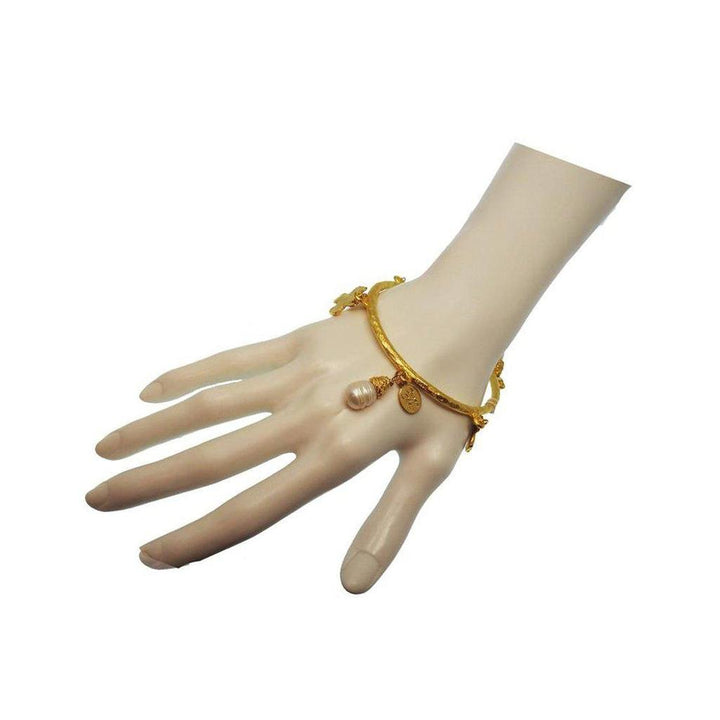 Gold bangle bracelet featuring a pearl and cross charms.