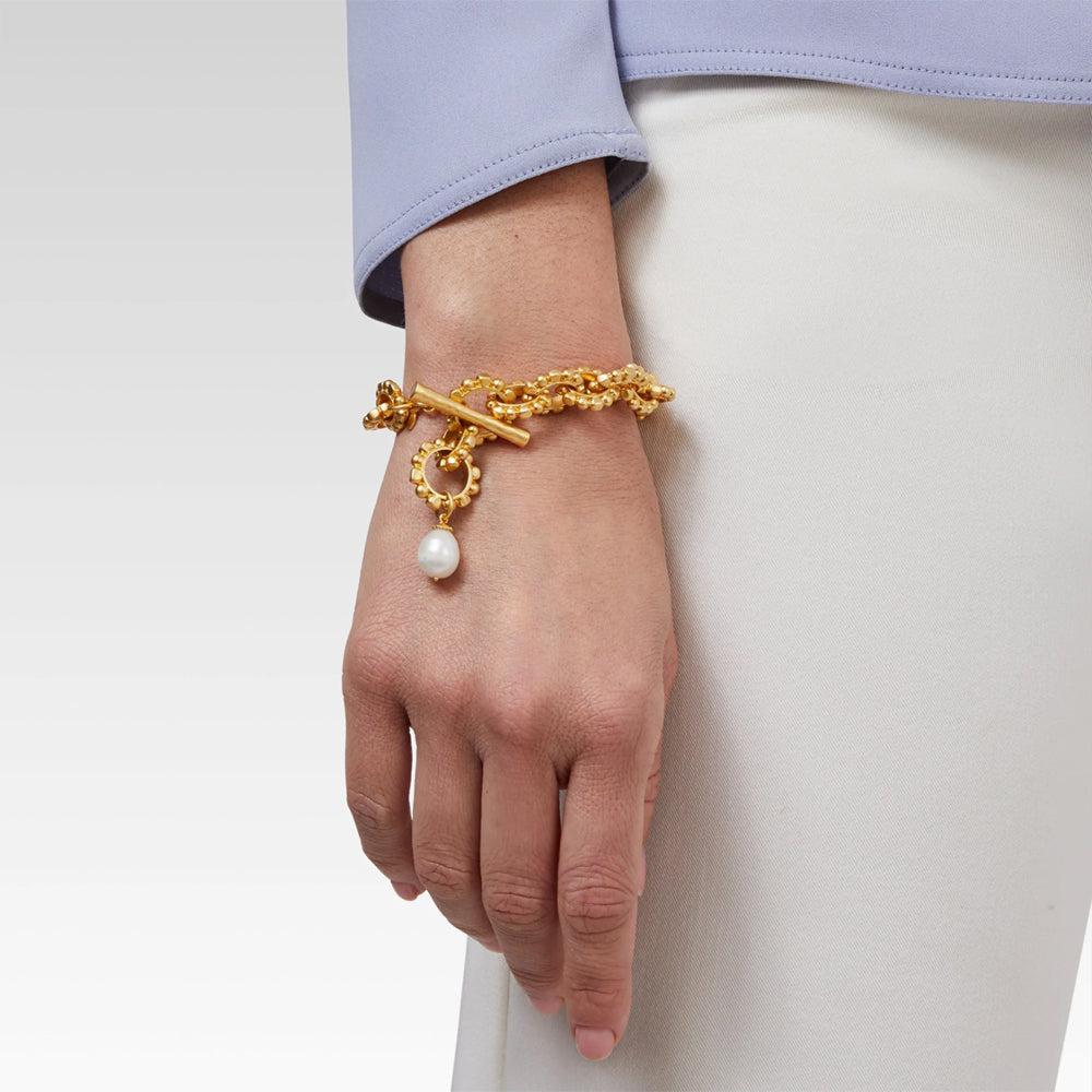 Gold toggle bracelet with textured chain and pearl detail on a wrist.