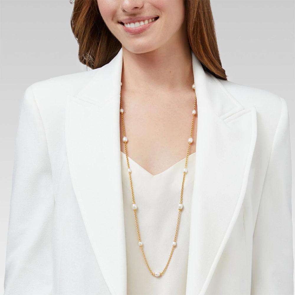 Gold chain necklace featuring white pearls, shown on model wearing a white blazer.