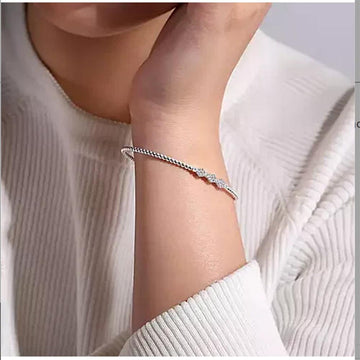 White gold bangle bracelet adorned with a cluster of diamonds, shown on a wrist.
