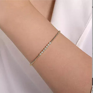 Delicate gold bangle featuring a row of sparkling diamonds, worn on a wrist.
