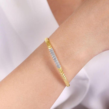 Gold chevron cuff bracelet adorned with diamonds, shown on a wrist.
