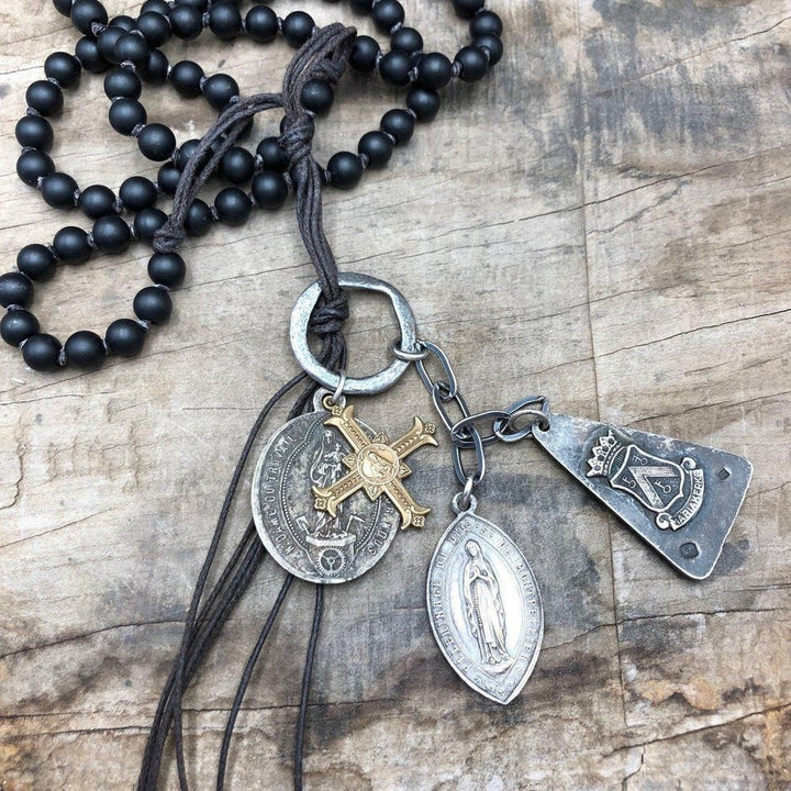 Multi-charm necklace featuring antique medallions and a black beaded cord, displayed on wood.
