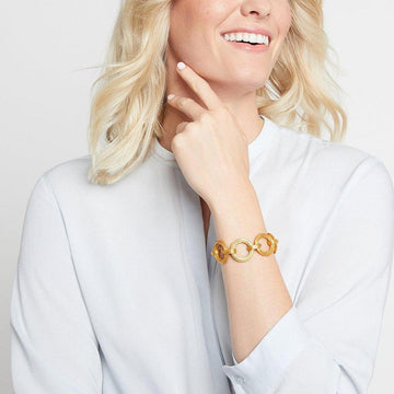 Gold interlocking circle bracelet on a woman's wrist, light blue shirt background.
