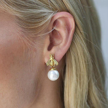 Gold bee charm dangling from a pearl earring.
