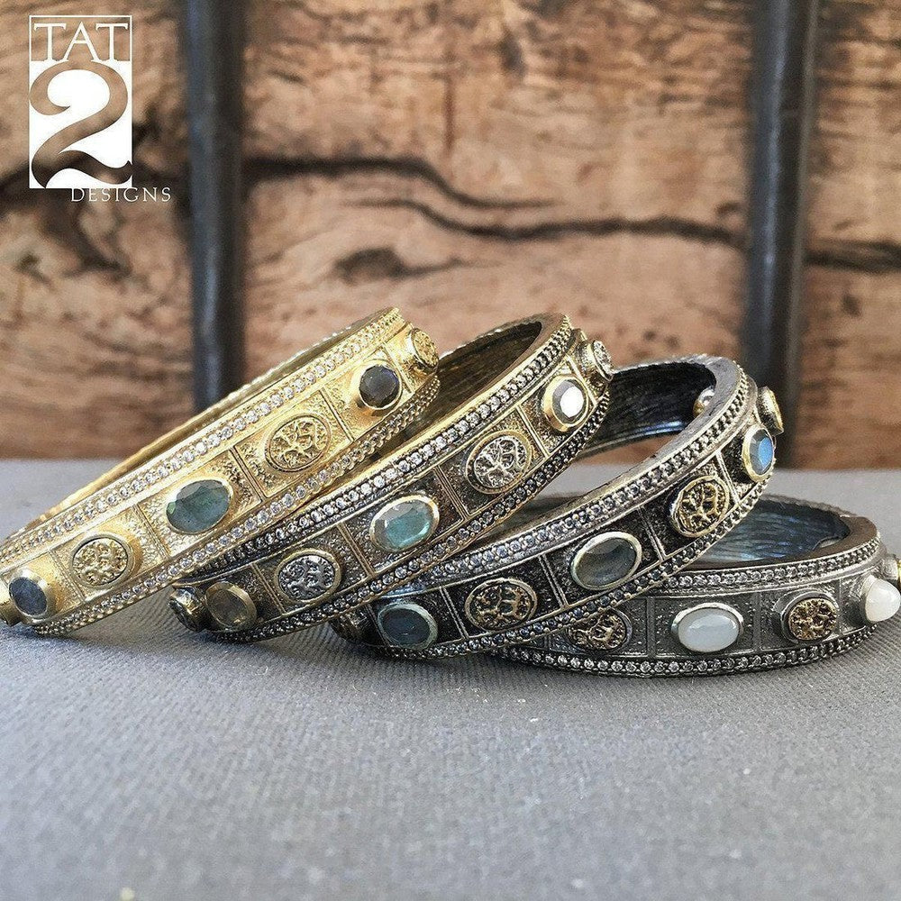 Elegant hinged oval bangles, adorned with gemstones and intricate detailing, displayed against a rustic wooden backdrop.
