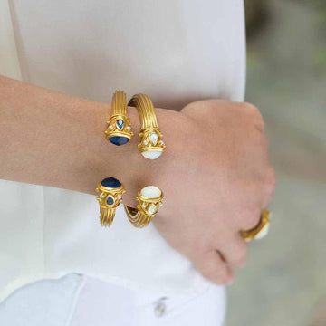Gold cuff bracelets adorned with blue and white gemstones, elegantly worn on a wrist.
