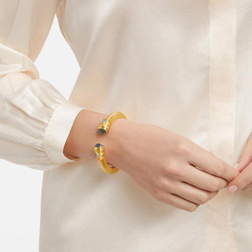 Gold cuff bracelet with dark blue gemstones, shown on a wrist.
