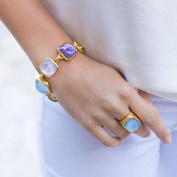 Gold chain bracelet featuring pastel gemstone links on a wrist.
