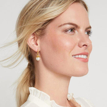 Gold hoop earrings with a dangling pearl charm, worn by a blonde woman.
