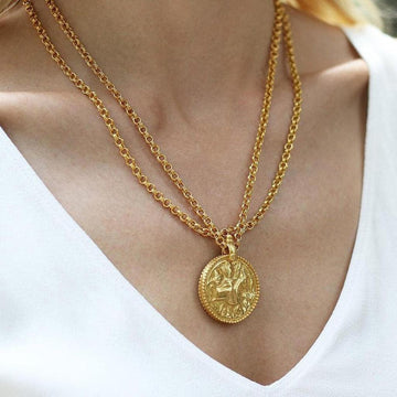 Gold coin pendant necklace with intricate detailing, worn on a white top.
