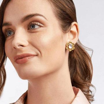 Gold flower-shaped stud earrings with a pearly center, worn by a woman.
