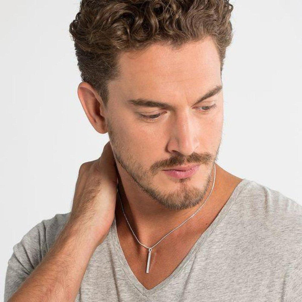 Man wearing a simple silver bar pendant necklace.
