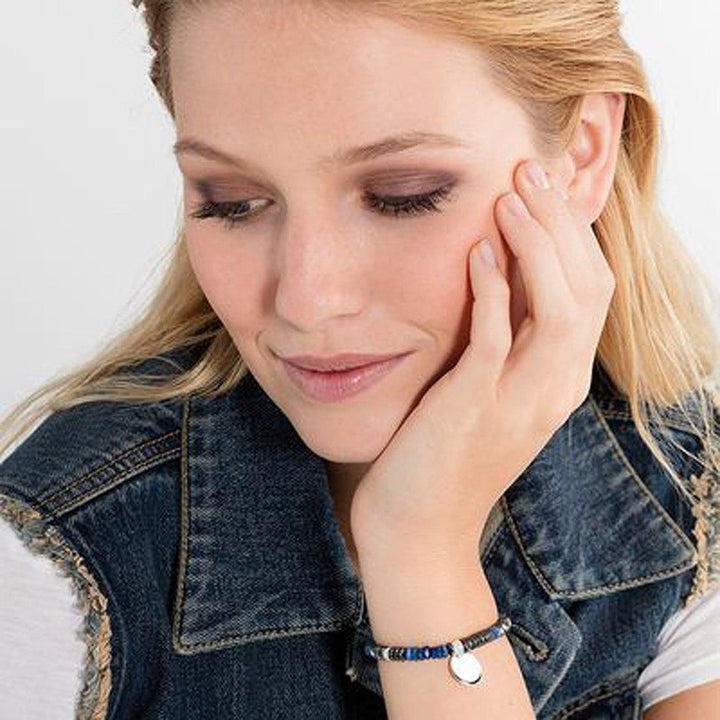 Woman's wrist wearing beaded bracelet with engravable charm; denim jacket backdrop

