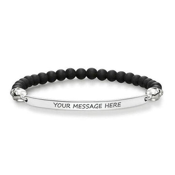 Black beaded bracelet with skull accents and engravable silver bar.
