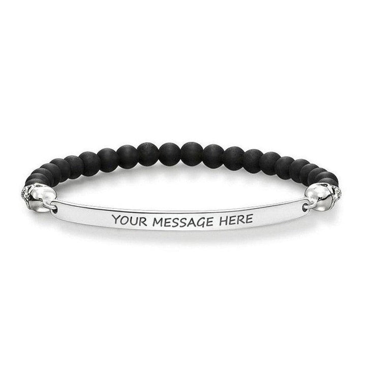 Black beaded bracelet with skull accents and engravable silver bar.

