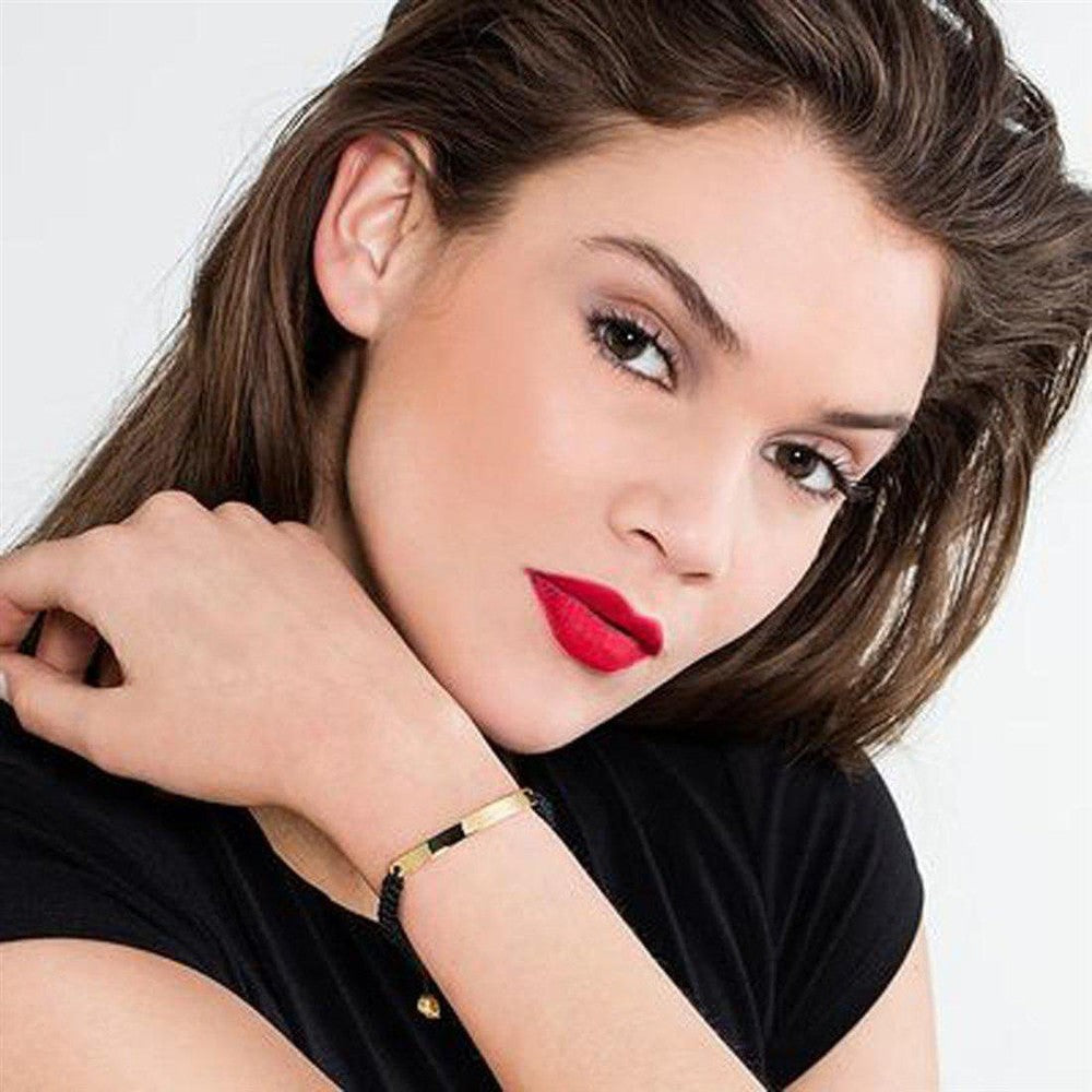 Woman's wrist showcasing a gold bar and black cord bracelet.

