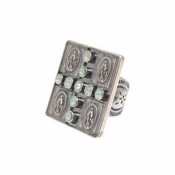 Square statement ring featuring a cross pattern of pale green stones, set against an antique silver-toned band with religious medallions.
