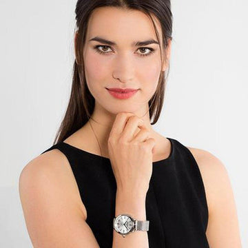 Woman's silver mesh watch with white face, elegantly displayed.
