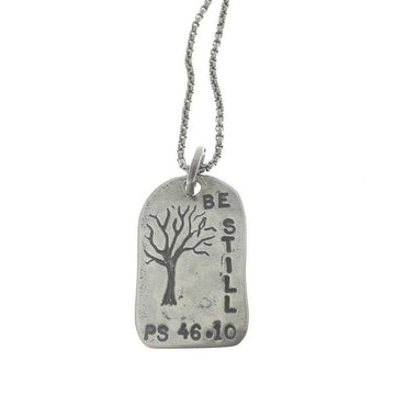 Silver "Be Still" necklace featuring a tree etching and Psalm 46:10.
