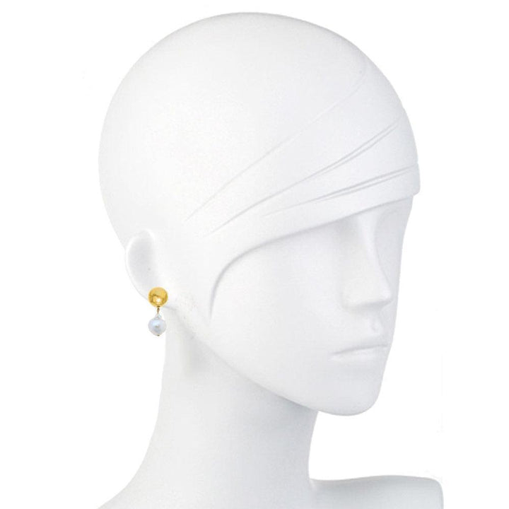 Elegant gold and pearl dangle earrings on a mannequin.
