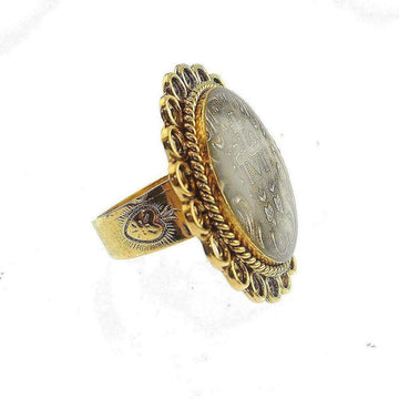 Gold statement ring featuring an oval coin-like centerpiece with ornate detailing.

