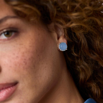 Round light blue faceted crystal stud earring in a silver bezel setting worn on an earlobe.