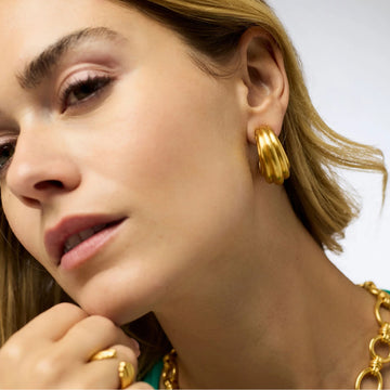 Model wearing a small, brushed 24K gold-plated ribbed hoop earring on a pierced ear.