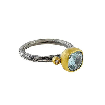 Light blue topaz gemstone ring with gold and oxidized silver band, featuring a small diamond accent.
