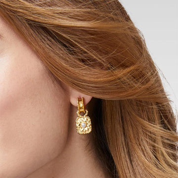Gold hoop earrings with a square pearl charm, worn against auburn hair.
