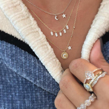 Layered gold necklaces featuring celestial-inspired pendants, styled on a textured sweater.
